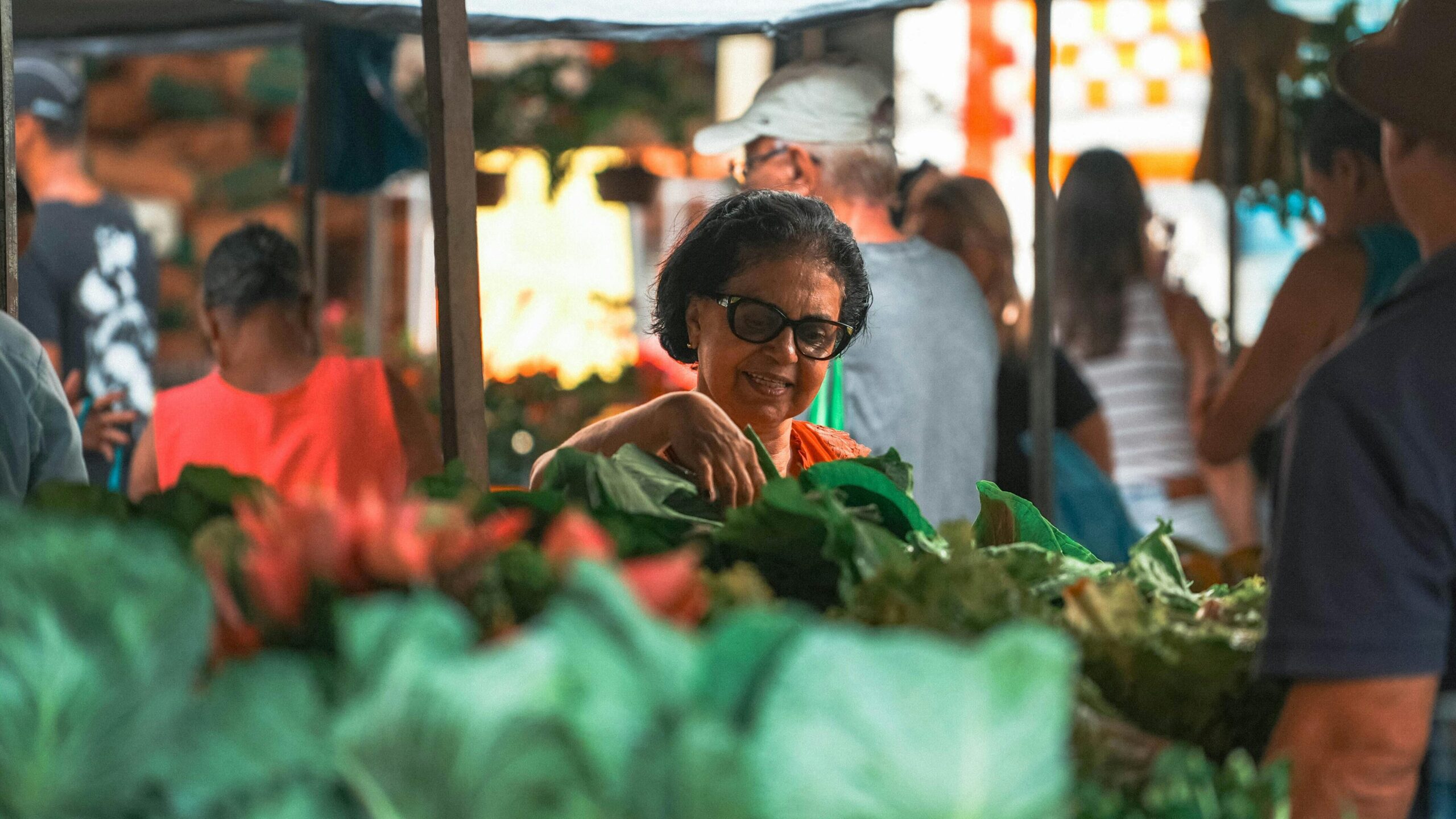 Senior woman browsing fresh greens at a vibrant outdoor market in Espírito Santo, Brasil.